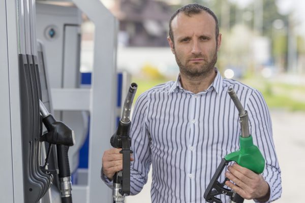 Homme mécontent à la station essence qui tient deux pompes différentes